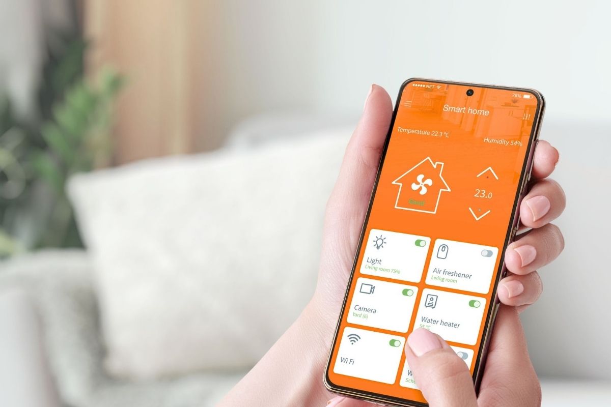 Close-up of a hand holding a smartphone displaying a smart home management app with controls for lighting, air conditioning, and other connected devices