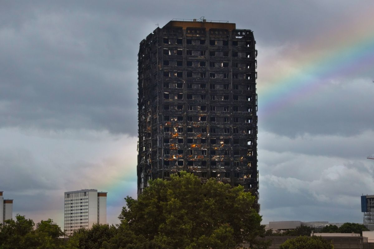Charred remains of Grenfell Tower in London, a stark reminder of the lives tragically lost and the urgent need for improved building safety regulations in the UK, with a faint rainbow symbolising hope for change.