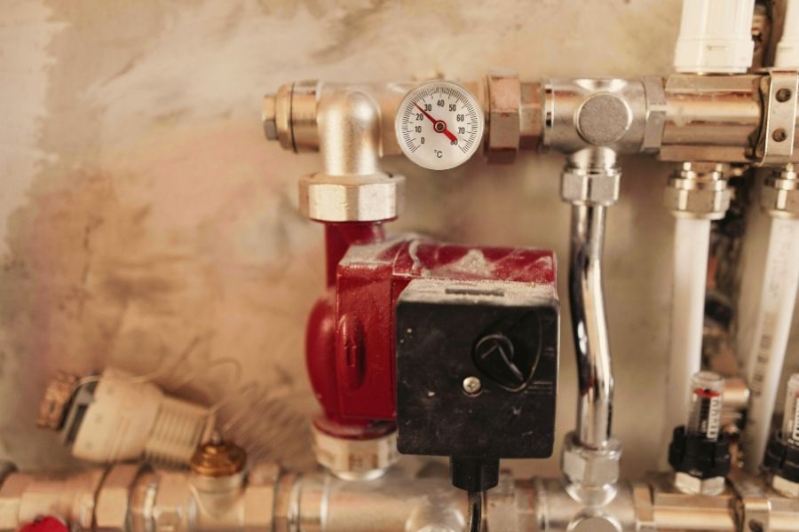 Steel pipes with a red pressure pump and a pressure gauge displaying temperature in a commercial facility.